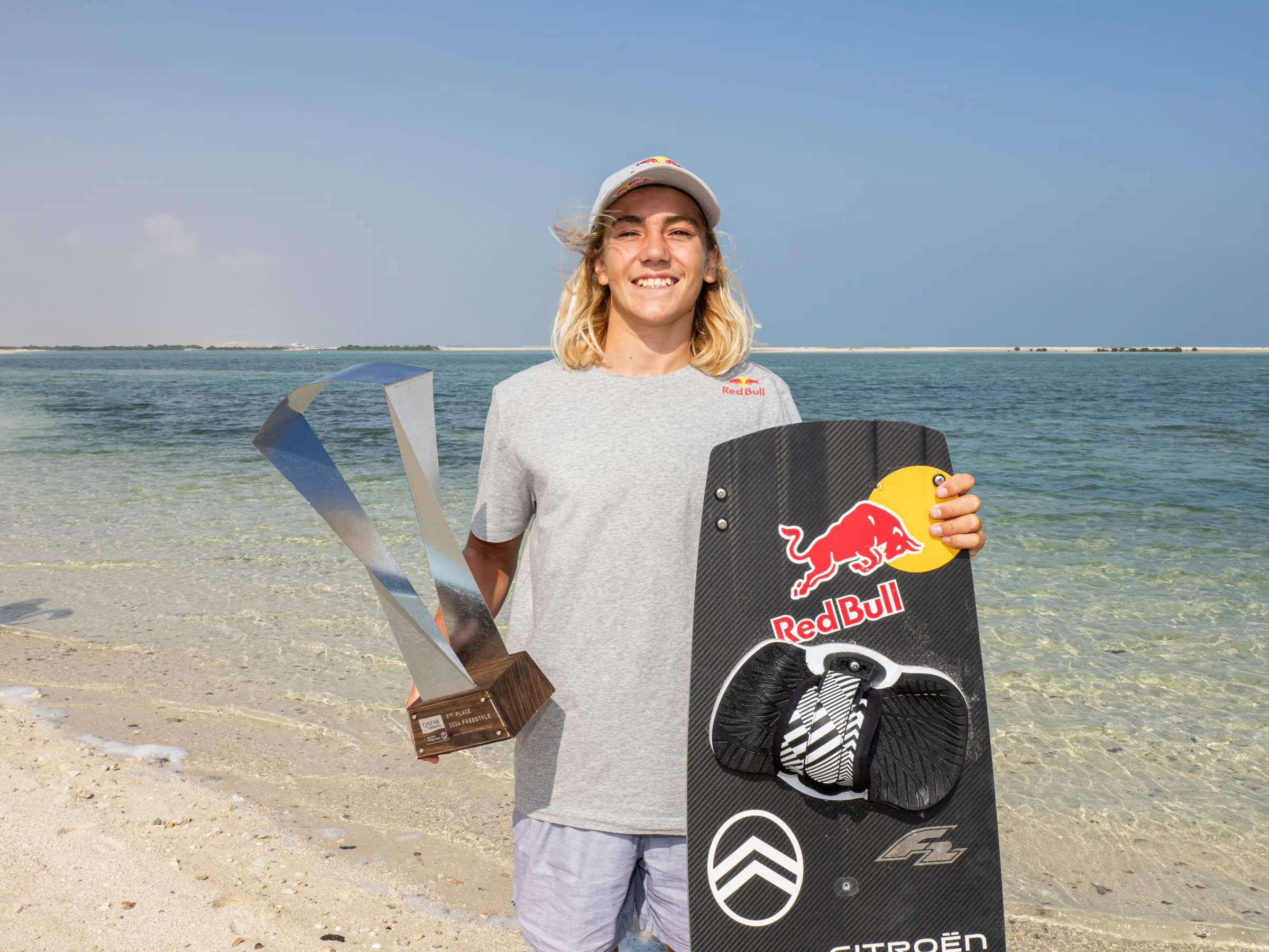 Finn Flügel with a trophy and his Red Bull board on the beach at the GKA World Cup in Doha, 2024