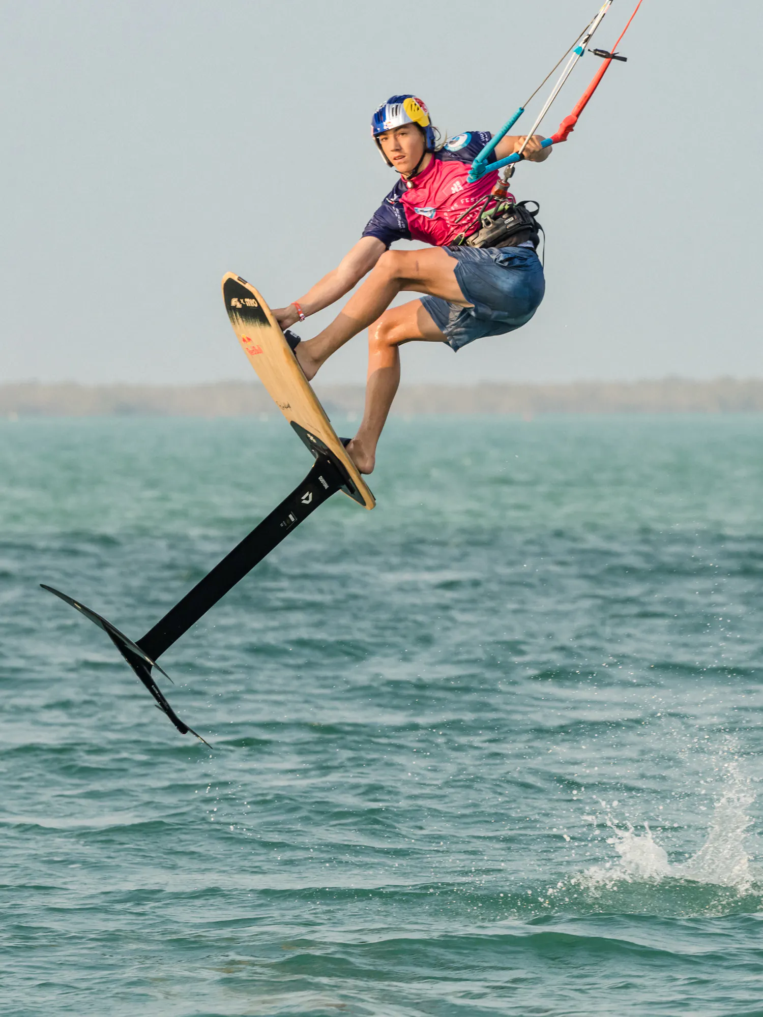 Finn Flügel airborne on his hydrofoil board, one hand grabbing the board, with the foil clear of the water below