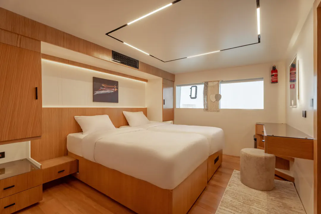 Cabin with two beds pushed together, a window to the sea and a desk