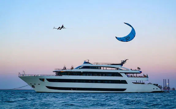 Finn in mid-air above a safari yacht at dusk, his blue kite high above the sea