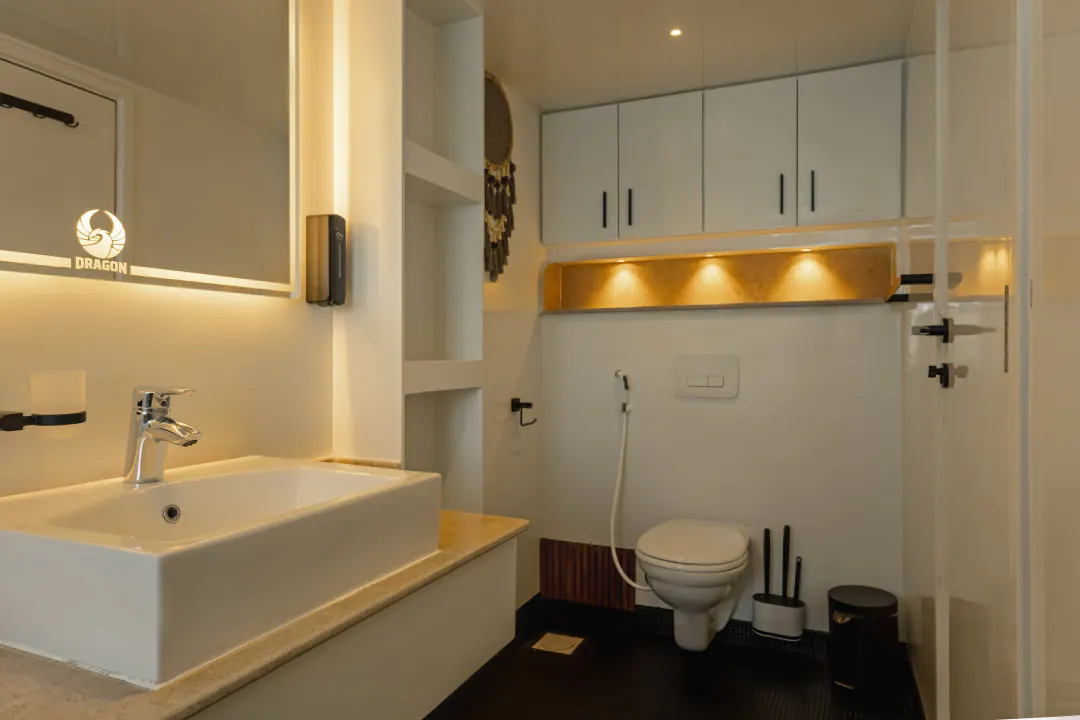 The cabin’s bathroom with a washbasin, a toilet and a shower behind a glass door, the DRAGON logo in the mirror