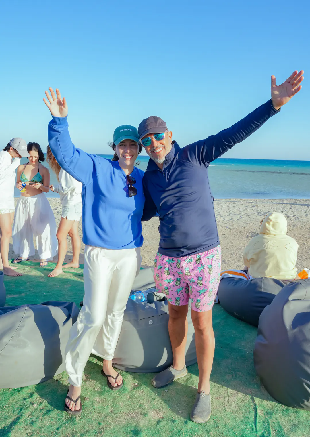 A couple on the beach throwing their arms up and laughing, the turquoise sea behind them
