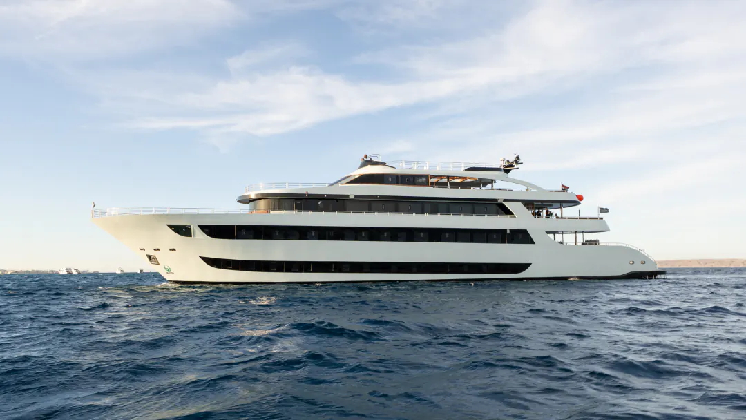 The DRAGON, a white multi-deck safari yacht, at sea under a blue sky