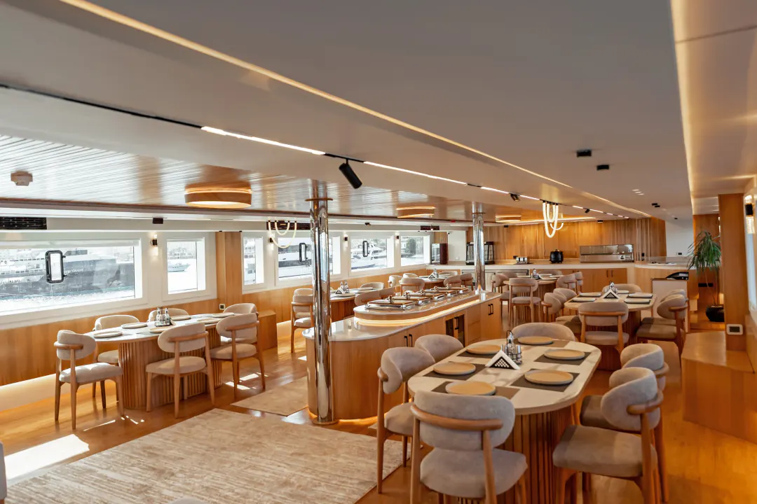 The restaurant on board: laid tables with pale upholstered chairs under a wooden ceiling, windows on both sides