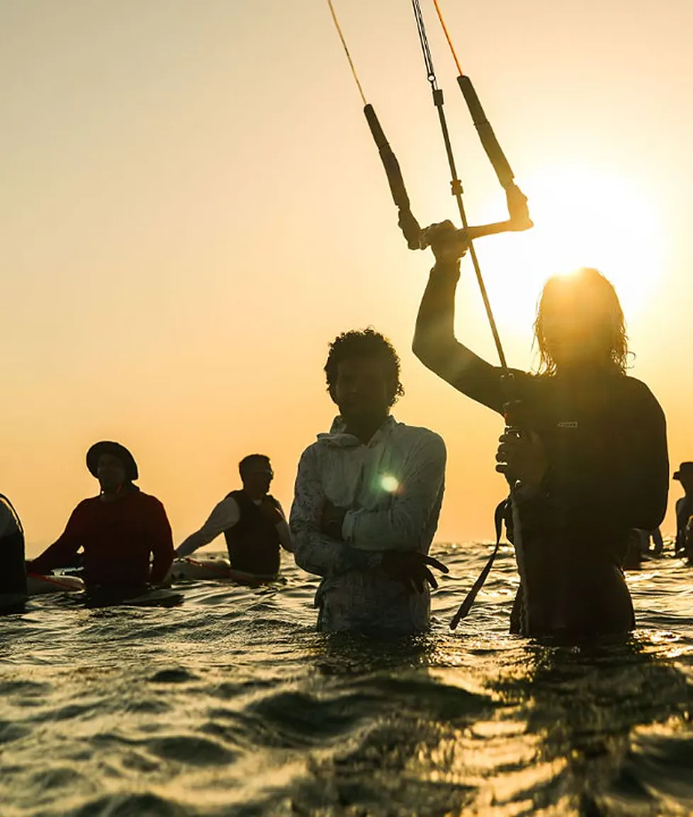 Kiters standing in the water against the evening sun